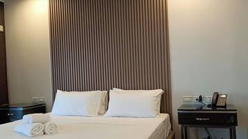 Una habitación de hotel con cama, mesita de noche y teléfono, y una pared con líneas verticales.