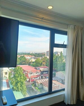 Quarto com uma grande janela, televisão de tela plana e controle remoto sobre uma mesa.
