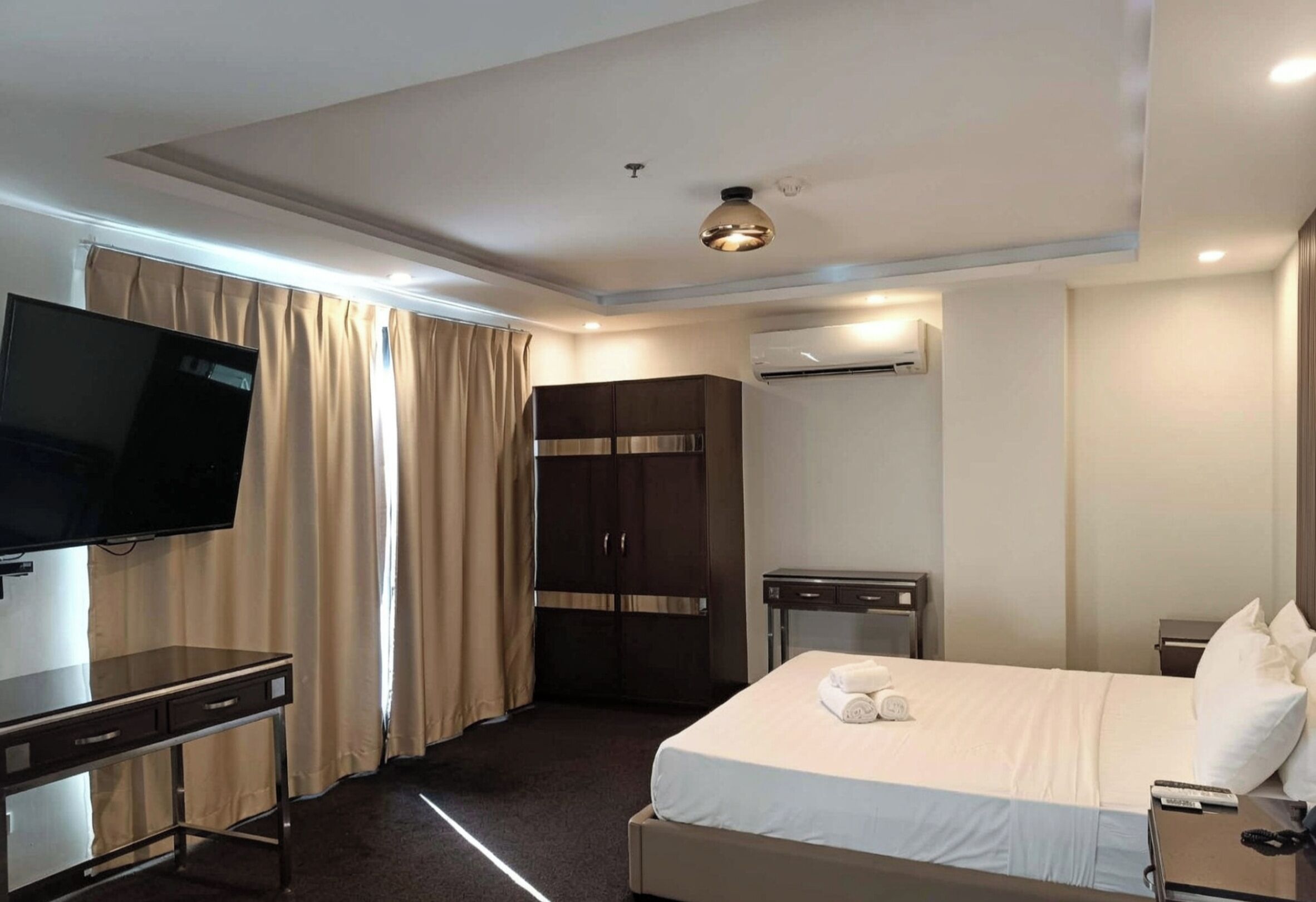 Een hotelkamer met een bed, een televisie, een kledingkast, een airconditioning en een bureau.