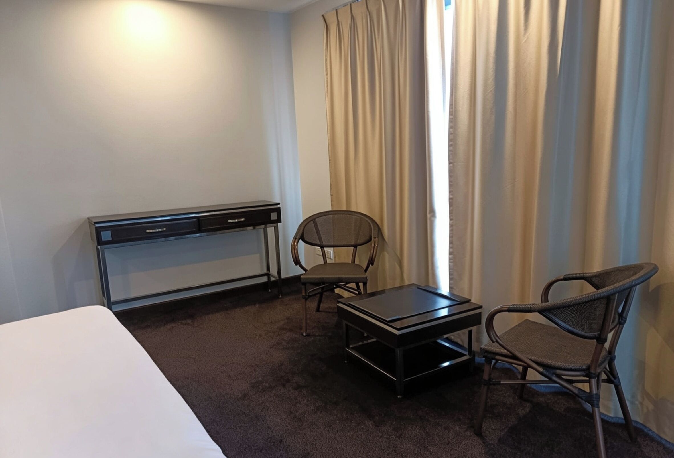 Una habitación de hotel con una cama, un escritorio, dos sillas y una ventana con cortinas.