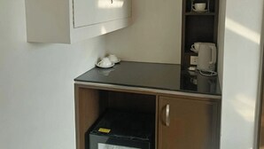 A corner kitchenette with a cabinet, a small shelf with cups and glasses, and a coffee maker. - The Fields Palace Hotel Premier (Angeles City)