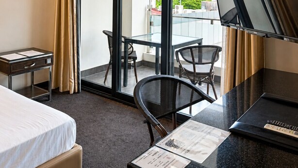 A hotel room with a bed, a desk with a computer, a chair, a small table, and a balcony with a glass door. - The Fields Palace Hotel Premier (Angeles City)