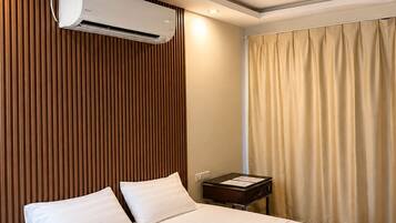A hotel room with a bed, an air conditioning unit, a nightstand, and a window with curtains.