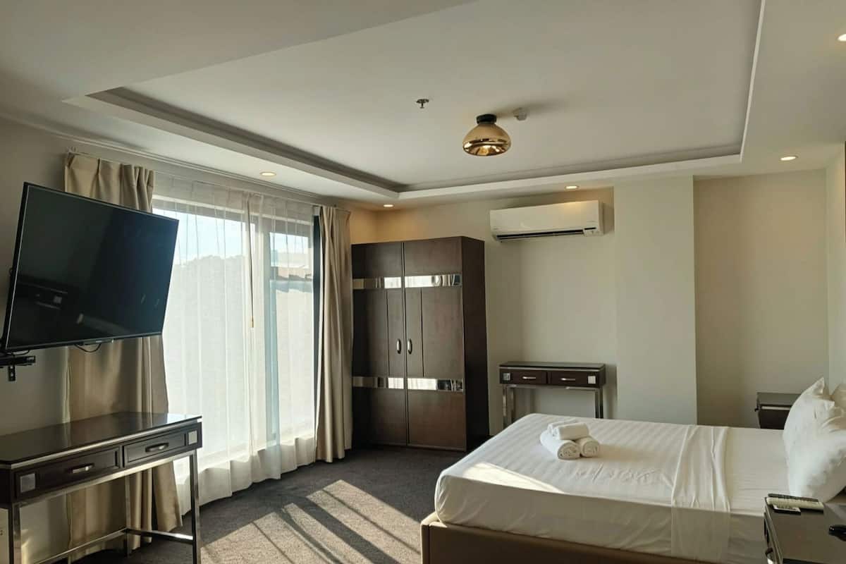Habitación de hotel con cama, televisor, armario, escritorio y ventana con cortinas.
