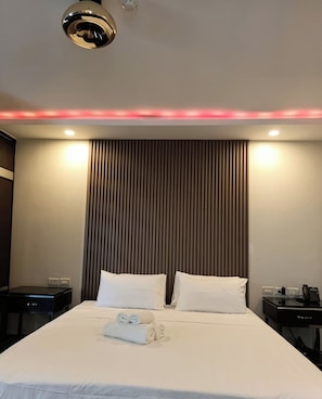 Una habitación de hotel con una cama, dos mesitas de noche, una lámpara de pared y una lámpara del techo.
