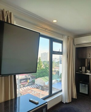 Habitación de hotel con un ventanal grande, una televisión de pantalla plana, un mando a distancia sobre un escritorio, una cafetera y un equipo de aire acondicionado.