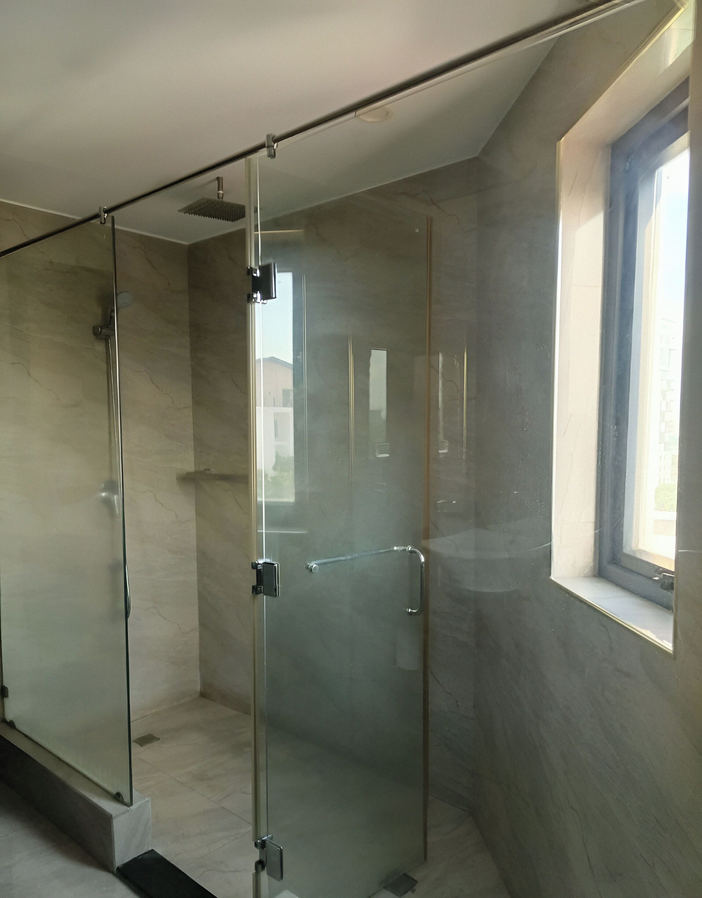 Une salle de bain moderne avec une douche à l’italienne en verre, une fenêtre et un sol en marbre.