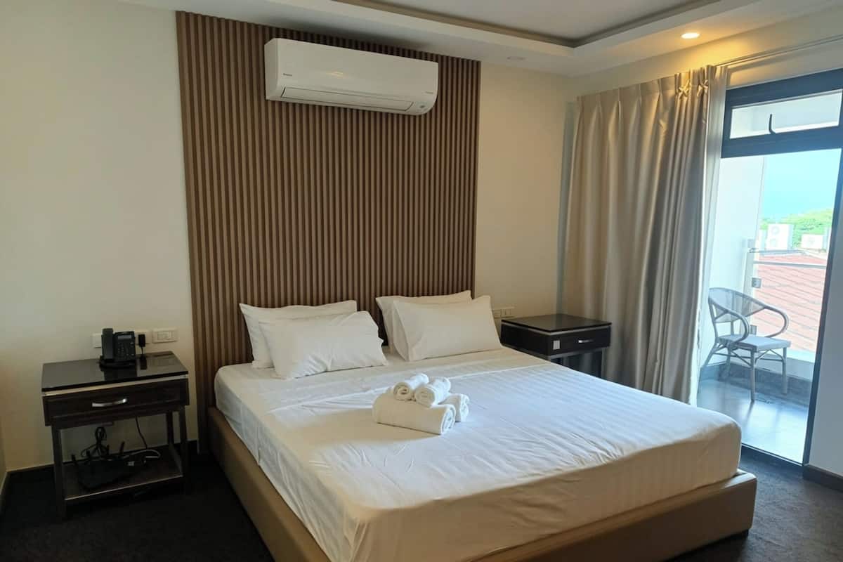 Habitación de hotel con cama, mesita de noche con teléfono, aire acondicionado instalado en la pared y vistas a través de una puerta de cristal.
