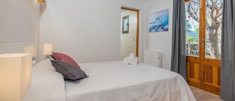 A bedroom with a bed, a nightstand, a lamp, a window with curtains, a radiator, and a painting on the wall.