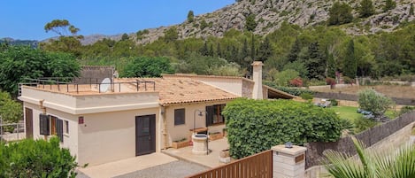 Una casa de dos pisos con techo de tejas, un balcón y un jardín con diversas plantas y un pequeño estanque.