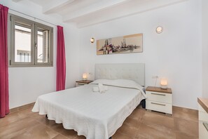 A bedroom with a bed, two bedside tables, a nightstand, a window with curtains, and a wall-mounted painting. - Central Townhouse with Pool, Pollença (Pollensa / Pollença)