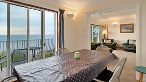 A dining area with a view of the sea, a balcony with chairs, and a living room with a sofa and a painting. - Lavish Sea-view Holiday Home in Seaton (Torpoint)