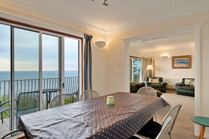 A dining area with a view of the sea, a balcony with chairs, and a living room with a sofa and a painting. - Lavish Sea-view Holiday Home in Seaton (Torpoint)
