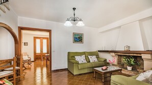 A living room with a green sofa, wooden chairs, a marble coffee table, a fireplace, and a painting on the wall. - Pollensa Villa with Private Pool (Pollensa / Pollença)