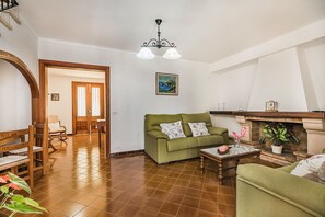 A living room with a green sofa, wooden chairs, a marble coffee table, a fireplace, and a painting on the wall. - Pollensa Villa with Private Pool (Pollensa / Pollença)