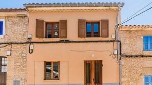 A two-story building with a stone facade, a wooden door with a metal gate, and a window with a car reflection. - Pollensa Villa with Private Pool (Pollensa / Pollença)