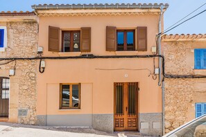 A two-story building with a stone facade, a wooden door with a metal gate, and a window with a car reflection. - Pollensa Villa with Private Pool (Pollensa / Pollença)