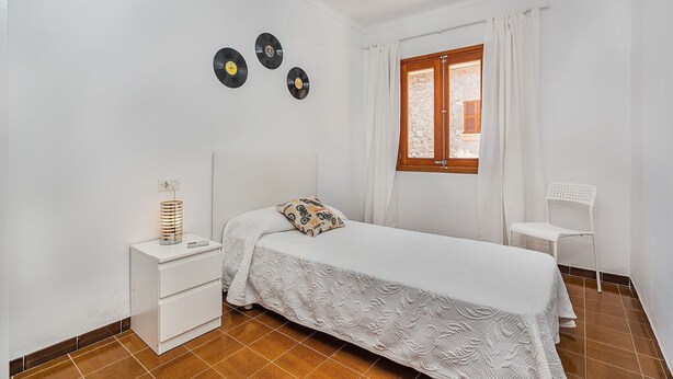 A bedroom with a bed, a nightstand, a chair, a window with curtains, and three wall-mounted records. - Pollensa Villa with Private Pool (Pollensa / Pollença)