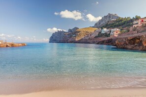 A coastal beach with clear water, rocky cliffs, and buildings on the hillside. - Pollensa Villa with Private Pool (Pollensa / Pollença)