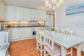 A kitchen with white cabinets, a dining table with chairs, a chandelier, and a painting on the wall. - Beach Chalet with Pool for 6 (Alcudia)