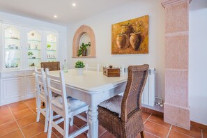 A dining area with a white table and chairs, a glass cabinet with decorative items, a painting above the table, and a column on the right. - Beach Chalet with Pool for 6 (Alcudia)