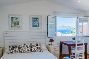 A bedroom with a bed, a nightstand, a desk, and a chair. There are two framed pictures on the wall and a window with a view of the sea. - Beach Chalet with Pool for 6 (Alcudia)