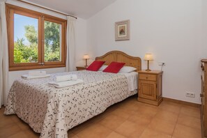Ein Schlafzimmer mit einem hölzernen Bett, zwei Nachttischen mit Lampen, einem Fenster mit Vorhängen und einem gerahmten Bild an der Wand.