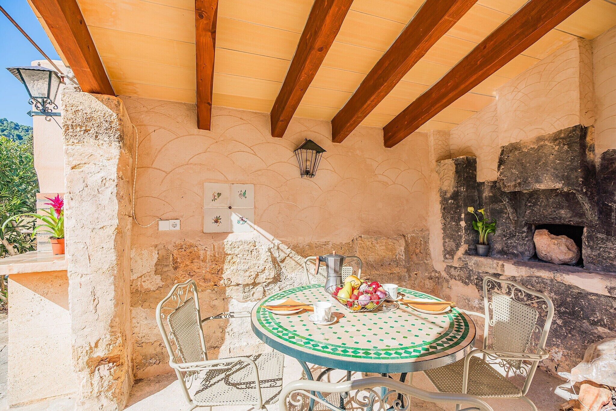 An outdoor patio with a round table, chairs, a coffee pot, and a stone oven.