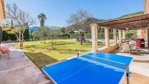 A blue ping pong table in a sunny outdoor area with a pergola, a barbecue, and a pool in the background. - Pollensa Villa with Private Pool (Pollensa / Pollença)