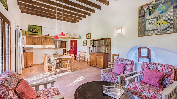 A spacious living area with a dining table, chairs, and a sofa. There is a kitchen area with wooden cabinets and a refrigerator. - Pollensa Villa with Private Pool (Pollensa / Pollença)
