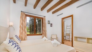 A bedroom with a bed, a window with curtains, a bedside table, a wall-mounted lamp, and a door with a ladder. - Pollensa Villa with Private Pool (Pollensa / Pollença)