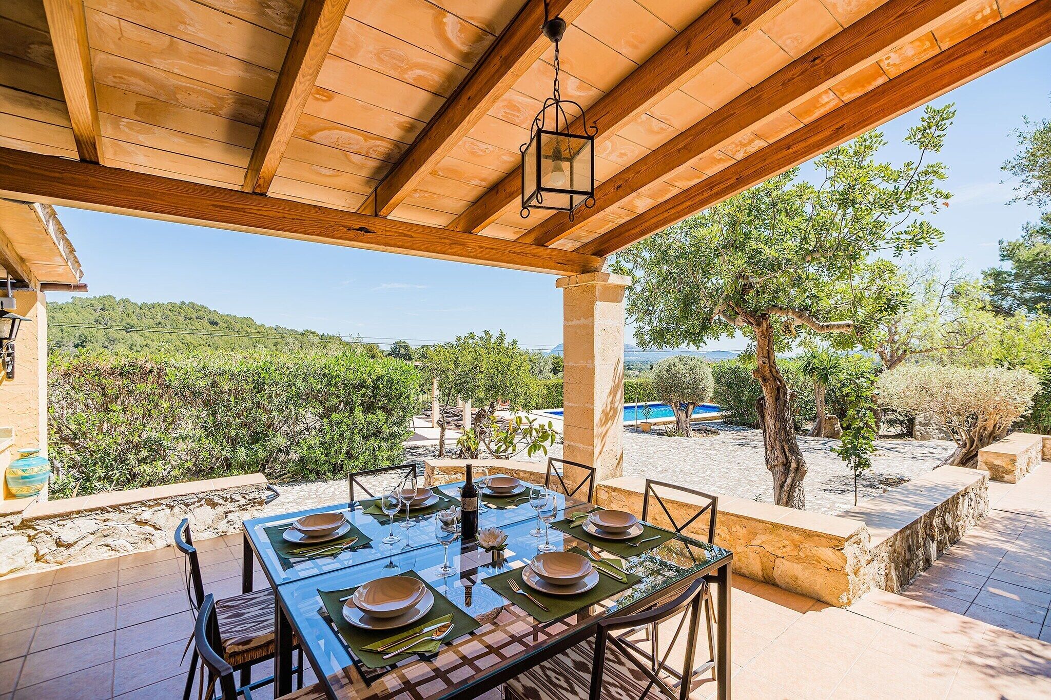 Un espace de restauration en plein air avec une table dressée pour quatre personnes, offrant une vue sur une piscine et un paysage montagneux.