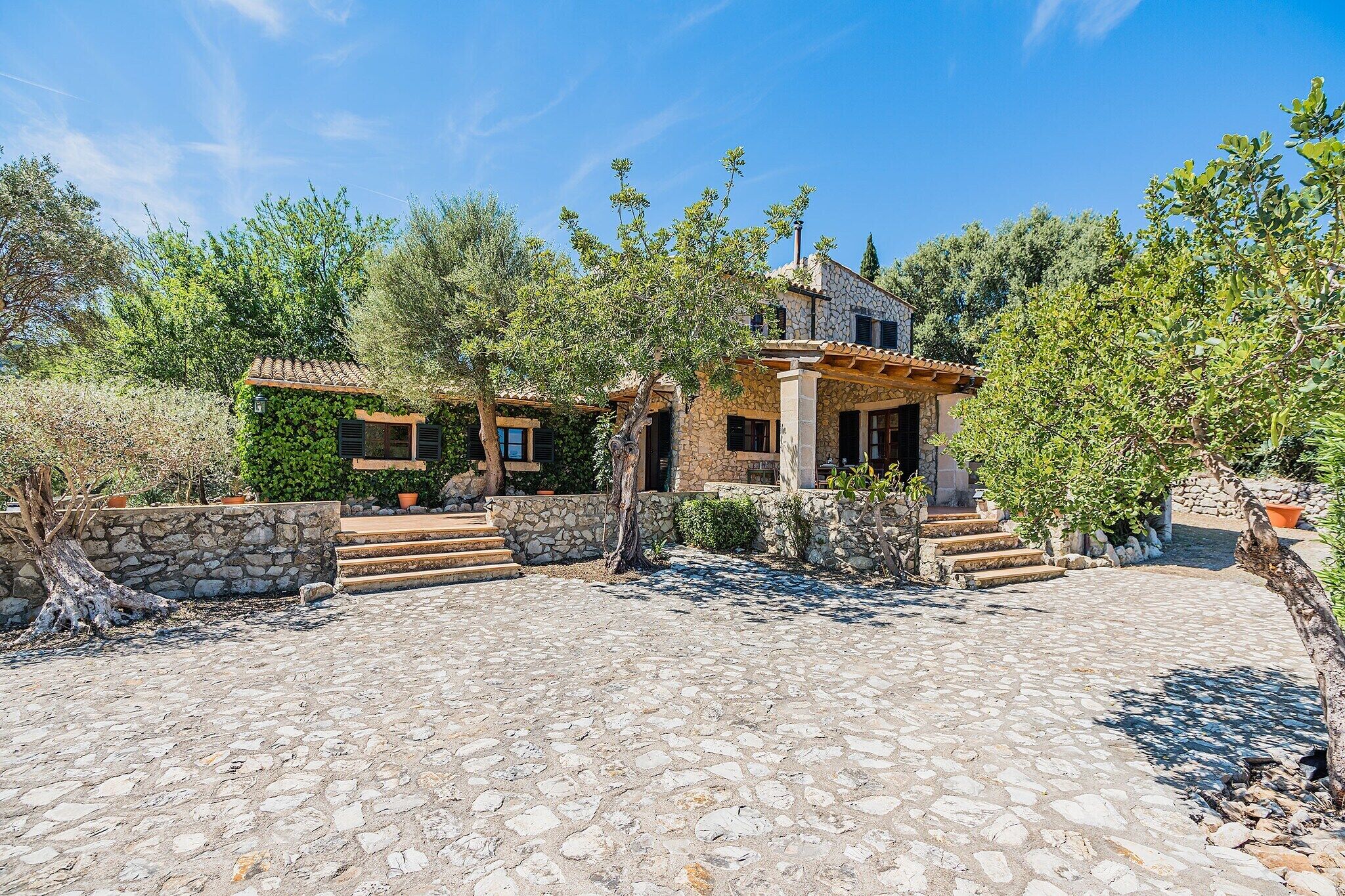 A stone building with a tiled roof, surrounded by trees and a cobblestone courtyard.