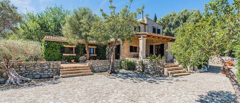 A stone building with a tiled roof, surrounded by trees and a cobblestone courtyard.
