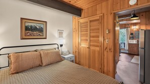 Una camera da letto con un letto, un comodino, un quadro e porte in legno che danno su un angolo cottura.