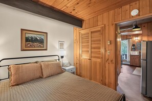 Une chambre à coucher comprenant un lit, une table de chevet, un tableau et des portes en bois donnant sur un espace cuisine.