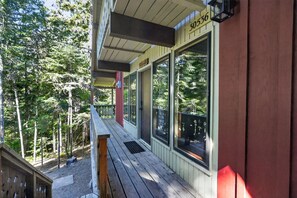 A wooden deck with a metal railing, large windows, and a number sign indicating the property address.