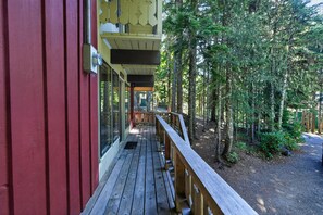 A wooden deck with a railing, leading to a building with a red facade and a covered porch. - Government Camp Cabin | Fireplace & Balcony (Government Camp)