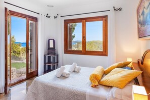 A bedroom with a bed, two windows, a dresser, and a view of the sea. - 5-Bed Villa, Two Pools, Puerto Pollença (Pollensa / Pollença)