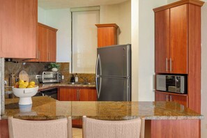 A kitchen with wooden cabinets, a stainless steel refrigerator, a microwave, a toaster, and a granite countertop. - Boho 2BR Retreat - Ocean View Terrace & Pool (Palmas del Mar)