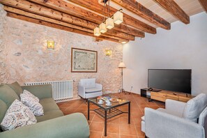 Ein Wohnzimmer mit Steinwand, einem gerahmten Stadtplan, einer Couch, einem Sessel, einem Couchtisch, einem Fernseher und einer Heizung.