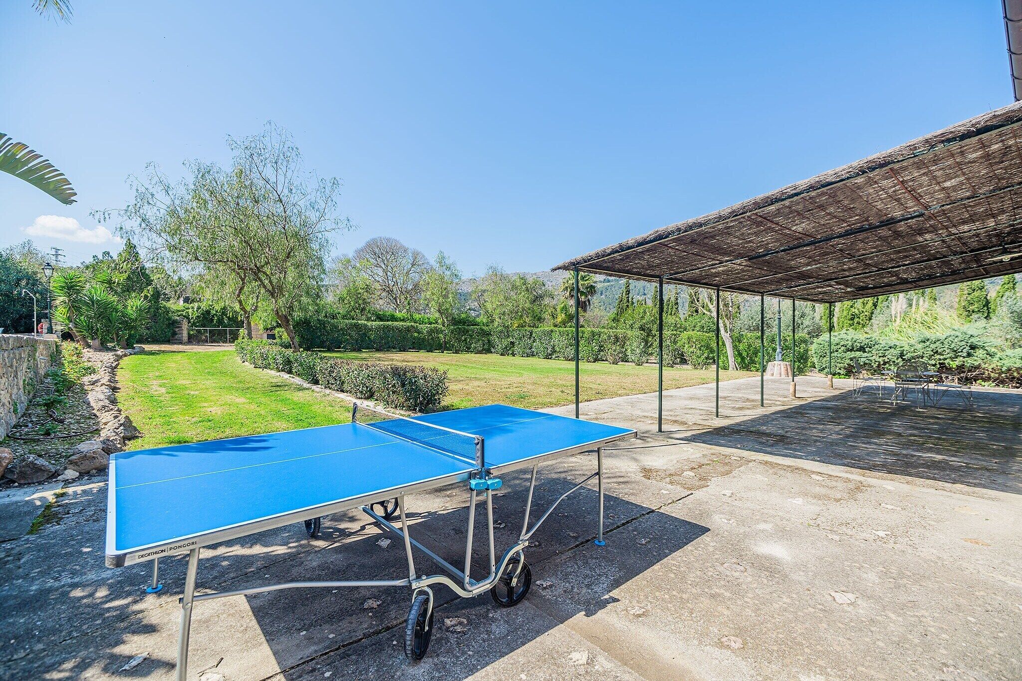 An outdoor ping pong table set up in a garden area with a pergola structure in the background.