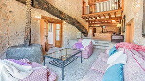 A rustic interior with stone walls, wooden beams, a glass coffee table, and checkered sofas. - Historic Villa with Mountain Views, Mallorca (Pollensa)