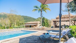 A pool area with lounge chairs and a table, surrounded by stone buildings and palm trees. - Historic Villa with Mountain Views, Mallorca (Pollensa)