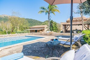 Ein Poolbereich mit Liegestühlen und einem Tisch, umgeben von Steinbauten und Palmen.