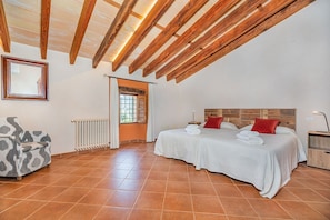 Ein Schlafzimmer mit zwei Betten, einem Heizkörper, einem Fenster mit Vorhängen, einem Sessel und einer Holzbalkendecke.