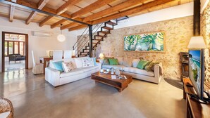 A spacious living area with a large sofa set, a coffee table, and a stone wall with a tropical painting. - Villa near Pollença Town Centre (Pollensa / Pollença)