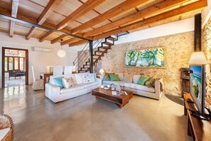 A spacious living area with a large sofa set, a coffee table, and a stone wall with a tropical painting. - Villa near Pollença Town Centre (Pollensa / Pollença)