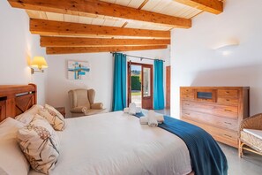 A bedroom with a bed, a chair, a wooden dresser, and a door leading to a garden. - Villa near Pollença Town Centre (Pollensa / Pollença)