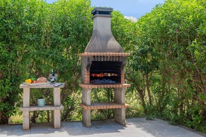 An outdoor brick-built barbecue grill with a chimney, surrounded by greenery. - Nice villa near centre of Pollença (Pollensa / Pollença)